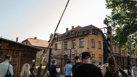 Ein Backsteinhaus, davor ein Eingangstor, oben ragt der Schriftzug: Arbeit macht frei.