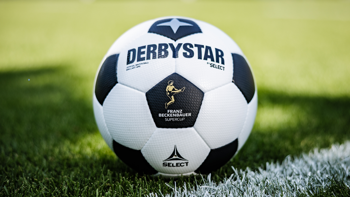 Der exklusive Supercup-Spielball von DERBYSTAR im klassischen Schwarz-Weiß-Design mit dem offiziellen Wettbewerbslogo, liegend auf dem grünen Rasen eines Spielfelds.