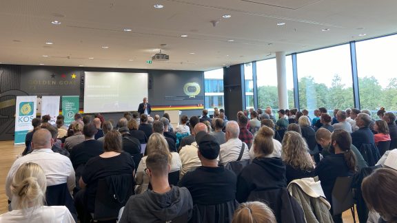 Personen sitzen in einem Tagungsraum und hören einem Redner zu.