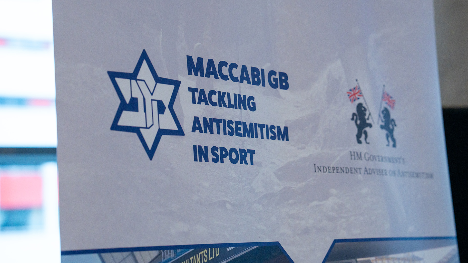 Banner mit der Aufschrift „Maccabi GB Tackling Antisemitism in Sport“ und Logos, darunter das britische Regierungswappen.
